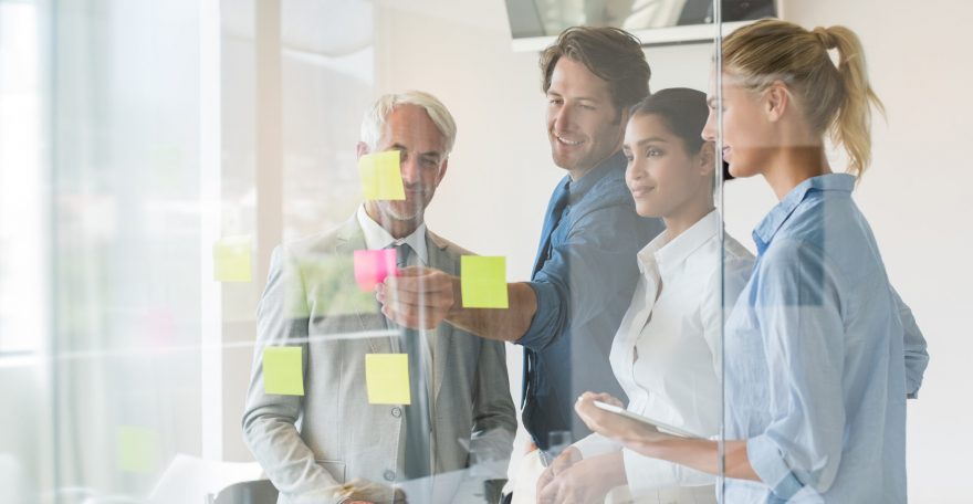 Smiling businessmen and businesswomen looking at sticky notes in board room. Creative business team looking at adhesive notes in office. Successful business teamwork discussing over sticky notes.